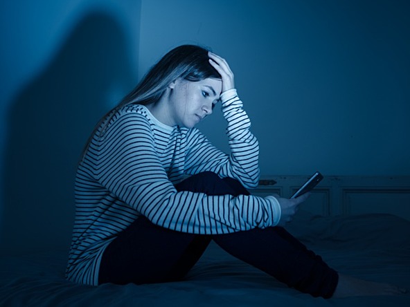 young woman looking distressed while looking at phone in dark room